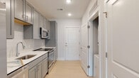 Located at 55 Gardner Dr on Hilton Head Island, South Carolina, this single-floor unit offers a thoughtfully designed layout with modern finishes throughout. The kitchen is a standout feature, outfitted with gray shaker-style cabinetry, white quartz countertops, a subway tile backsplash, and a full suite of stainless steel appliances including a range, over-the-range microwave, and refrigerator. A stacked washer and dryer unit is conveniently tucked into a dedicated laundry closet just off the kitchen. Light wood-look flooring runs through the main living areas, lending a clean, contemporary aesthetic, while recessed lighting keeps the space bright throughout. The living area benefits from multiple windows that bring in natural light and offer views of the surrounding community. Bedrooms include a carpeted room with a ceiling fan and windows, as well as an additional room with light hardwood flooring and a wide window bank. The bathroom is finished with large-format light tile flooring, gray cabinetry with a white countertop, a framed mirror, and a glass-enclosed walk-in shower. The overall design palette of soft grays, whites, and natural wood tones creates a cohesive and modern atmosphere.