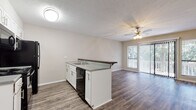 This single-floor residence offers a well-designed open-concept layout that seamlessly connects the kitchen and living area. The kitchen is equipped with white cabinetry, dark granite-style countertops, and a full suite of black appliances including a range, microwave, dishwasher, and refrigerator. A peninsula with a breakfast bar overhang provides additional counter space and casual seating, while a sink with ample workspace completes the functional design. The living area is bright and spacious, featuring durable hardwood-style plank flooring, a ceiling fan with light fixture, and large sliding glass doors flanked by windows that allow abundant natural light and provide access to a private outdoor balcony. The two bedrooms are carpeted for comfort, each featuring ceiling fans, natural light from windows, and closet storage. The primary bedroom includes a sliding-door closet with built-in shelving. The unit features two bathrooms: one with a standalone walk-in shower and hardwood-style flooring, and a second full bathroom with a tub-shower combination, white vanity, and matching flooring. Neutral wall tones and clean finishes throughout contribute to a fresh, move-in-ready atmosphere.
