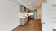 This single-floor studio unit is situated in a downtown location and offers a thoughtfully designed open-plan layout finished with contemporary materials throughout. Rich wood-tone vinyl plank flooring runs continuously across the living, sleeping, and kitchen areas, lending warmth and visual cohesion to the space.

The kitchen is a standout feature, outfitted with flat-front, light wood-grain cabinetry that extends to the ceiling for ample storage. A white quartz countertop and a classic white subway tile backsplash provide a clean, modern aesthetic, while a full suite of stainless steel appliances — including a refrigerator, electric range, built-in microwave, and dishwasher — ensures full functionality. Recessed lighting illuminates the workspace effectively.

The living and sleeping area is bright and open, with large double-pane windows that invite natural light and offer views of the surrounding downtown streetscape. A generous closet with built-in shelving provides practical storage.

The bathroom is finished to a high standard, featuring a wood-grain vanity with a white quartz countertop, an undermount sink, and a large mirror with contemporary overhead lighting. Wood-look flooring continues here, complementing the overall design. In-unit stacked laundry is conveniently accessible from the bathroom area. The unit's clean lines and neutral palette create a bright, functional living environment suited to urban living.