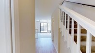 This two-story residence offers a thoughtfully designed layout across two levels, providing comfortable separation between living and sleeping areas. The main level welcomes you with light hardwood-style flooring that flows seamlessly through the entry and into the open living space. A striking staircase with white-painted wooden balusters and a dark handrail serves as an elegant focal point near the entryway.

The living area is bathed in natural light, courtesy of large sliding glass doors that open to an outdoor space, creating an airy and open atmosphere. Neutral warm tones on the walls complement the bright, clean aesthetic throughout. The generous proportions of the main living area lend a spacious feel well-suited for both everyday living and entertaining.

The home features two bedrooms, providing ample accommodation, along with a full bathroom and a convenient half bathroom — ideal for guests on the main level. The two-story configuration ensures privacy and clear zoning between the communal and private areas of the home.

Overall, the space exudes a clean, modern character with an abundance of natural light, a cohesive neutral color palette, and well-maintained finishes that make it move-in ready and highly livable.