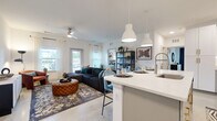 This thoughtfully designed 2-bedroom, 2-bathroom residence offers a cohesive open-concept layout that seamlessly connects the kitchen, dining, and living areas. The kitchen is a standout feature, showcasing white upper cabinetry and soft gray lower cabinets accented with gold hardware, under-cabinet lighting, stainless steel appliances, and a spacious island with a waterfall-edge countertop illuminated by modern pendant lights — perfect for casual dining or entertaining. The living room is bright and airy, benefiting from multiple windows that invite natural light, with a ceiling fan adding comfort. Both bedrooms are well-proportioned, each with ceiling fans, natural light from windows, and closet storage. The primary bedroom offers a calm, serene atmosphere with ample space. The two bathrooms are finished with sleek gray vanities, gold hardware, white quartz countertops, and polished fixtures — one featuring a glass-enclosed shower and the other a soaking tub. Consistent light-toned flooring flows throughout the entire residence, tying each room together with a clean, contemporary aesthetic. Two closets provide practical storage solutions. The overall ambiance is modern, bright, and refined.