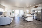 This two-floor residence is designed with a clean, contemporary aesthetic characterized by neutral tones, recessed lighting, and a seamless blend of wood-look flooring and plush carpet throughout. The main level centers around an open-concept layout where the living room, dining area, and kitchen flow together naturally, creating a spacious and well-lit communal space. Large sliding glass doors in the living area allow abundant natural light and provide access to an outdoor balcony, while additional windows frame views of the surrounding area. The kitchen is outfitted with white cabinetry, stainless steel appliances, and a center island with a light stone countertop that doubles as a breakfast bar with seating for multiple guests. A dedicated living space features wood-look flooring, elevated windows, and a built-in storage unit, adding functional depth to the layout. Bathrooms are finished with white vanity cabinetry, broad mirrors, and light countertops. The bedrooms are carpeted for comfort, each featuring ceiling fans, generous natural light from multiple windows, and notably tall ceilings that contribute to an airy, open atmosphere throughout the upper floor.