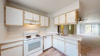 This single-floor residence offers a clean, functional layout designed for comfortable everyday living. The kitchen is equipped with white appliances, including an electric range, dishwasher, and refrigerator, complemented by light wood-framed cabinetry with white panel doors and continuous countertops. Wood-look flooring runs through the kitchen and utility areas, lending a cohesive, easy-to-maintain feel.

The living area is generously proportioned, featuring neutral carpet, a ceiling fan with light fixture, and an open sightline toward the kitchen. A sliding glass door leads to a private balcony overlooking a serene outdoor setting with mature trees and a water view, bringing natural light into the space.

The bedrooms are carpeted and well-sized, with one featuring direct access to a full bathroom and a spacious walk-in closet with built-in shelving. The bathrooms are finished with wood-look flooring, white vanities, and a tub-shower combination with sliding glass doors.

A dedicated utility area houses a stacked washer and dryer alongside the refrigerator, offering convenient in-unit laundry. Throughout, the residence maintains a bright, neutral palette that creates a clean and adaptable living environment.