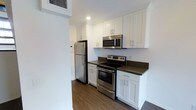 This two-floor residence offers a well-appointed layout designed for comfortable everyday living. The kitchen is a standout feature, showcasing a clean, modern aesthetic with white shaker-style cabinetry extending to the upper walls, providing generous storage throughout. Dark countertops offer a striking contrast against the bright cabinetry, while a full suite of stainless steel appliances—including a refrigerator, electric range, and over-the-range microwave—delivers a polished, functional workspace. Recessed lighting illuminates the kitchen, enhancing the crisp, contemporary feel of the space. Rich, dark hardwood-style flooring runs underfoot, adding warmth and visual depth to the interior. The two-floor configuration of this 1-bedroom, 1-bathroom space allows for a natural separation between living and private areas, contributing to a functional and organized floor plan. The overall design combines practical finishes with modern detailing, creating a cohesive interior that balances style and utility throughout.