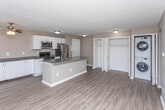 Located at 2359 Livernois Rd in Troy, Michigan, this single-floor unit offers a well-designed, open-concept layout that maximizes both functionality and comfort. The kitchen serves as the centerpiece of the living space, featuring crisp white cabinetry, dark granite countertops, a large central island with a built-in sink, and a full suite of stainless steel appliances including a refrigerator, range, and microwave. Wood-look luxury vinyl flooring runs throughout the main living and kitchen areas, complemented by a ceiling fan that adds to the airy feel of the space. The open living area flows seamlessly from the kitchen and includes an in-unit stacked washer and dryer, offering added convenience. The bedrooms are carpeted for comfort and each features neutral-toned walls and windows with vertical blinds that allow for natural light and outdoor views. The primary bedroom includes direct access to an en-suite bathroom. Two bathrooms serve the unit — one with a tub/shower combination and wood-look flooring, and a second with a clean, minimalist vanity and matching flooring. The overall palette of warm beige and grey tones throughout the unit creates a cohesive and inviting atmosphere.