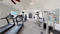 Located at 200 Ashbury Sq in Mebane, NC, this single-floor fitness center is thoughtfully designed to support a full range of workout routines. The space features soaring vaulted ceilings that create an open, airy atmosphere, complemented by multiple ceiling fans that help maintain comfortable airflow throughout. Neutral-toned carpet flooring runs across the facility, providing a clean and functional surface underfoot.

Natural light pours in through numerous windows positioned along the walls, offering views of the surrounding community and giving the space a bright, welcoming feel. A large wall-mounted mirror on one end visually expands the room while allowing users to monitor their form during workouts.

The fitness center is comprehensively equipped with a variety of cardio machines, including treadmills, elliptical trainers, and a stationary bike. Strength training needs are met with a multi-station cable machine, a dumbbell rack with a full range of free weights, adjustable benches, and a weight stack machine. Wall-mounted televisions are positioned strategically throughout the space to keep users entertained during their workouts.

The facility is accessible via a standard entry door and benefits from recessed and flush-mount lighting. The overall ambiance is clean, bright, and functional, making this fitness center a practical and inviting amenity for the Ashbury Square community.