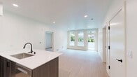 This well-appointed apartment in Vancouver, WA offers three bedrooms and three full bathrooms across a single thoughtfully designed floor. Light wood-tone flooring flows consistently throughout the space, creating a warm and cohesive aesthetic.

The kitchen is a standout feature, outfitted with dark espresso cabinetry, a classic white subway tile backsplash, quartz countertops, and a full suite of stainless steel appliances including a French door refrigerator, gas range, and built-in microwave. A peninsula with a waterfall-style dark base provides additional counter space and casual seating.

The living area benefits from large, floor-to-ceiling windows and a glass door that invite abundant natural light and offer pleasant views of the surrounding greenery. The bedrooms are clean and neutral, with light walls and wood flooring; one bedroom features a stylish black sliding barn door.

The three bathrooms are finished in a consistent modern style, featuring dark matte black fixtures, wood-toned vanities with white quartz countertops, and stone-textured surround walls. Two bathrooms include tub/shower combinations, while one offers a sleek walk-in glass shower. Clean white walls and recessed lighting complete the refined, contemporary aesthetic throughout.