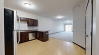 This single-floor unit offers a practical and comfortable layout across two bedrooms, one bathroom, and a dedicated laundry room. The open-concept kitchen and living area forms the heart of the unit, where light wood-style flooring runs throughout the kitchen zone before transitioning to plush gray carpet in the spacious living area. The kitchen is well-equipped with dark espresso cabinetry, granite-style countertops, stainless steel appliances including an electric range and dishwasher, and a peninsula that provides additional workspace and separation from the living area. The living room is generously sized, featuring neutral walls and a sliding glass door fitted with vertical blinds that allow natural light to filter in while providing access to an outdoor patio area.

Both bedrooms are carpeted and offer neutral tones, with the primary bedroom featuring a closet with built-in shelving. The full bathroom includes a dark-stained vanity, wood-style flooring, and a full tub-shower combination. A dedicated in-unit laundry room with side-by-side washer and dryer hookups adds everyday convenience to this functional and cohesive living space.