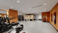 Located at 1010 Spring St NW in Atlanta's Midtown neighborhood, this fitness center offers a comprehensive, single-floor facility designed to support a wide range of workout routines. The space is thoughtfully laid out, with distinct zones dedicated to cardio training, strength and functional fitness, and recovery.

The cardio area is lined with a row of Life Fitness treadmills and upright bikes, positioned alongside a floor-to-ceiling slatted glass partition that allows natural light to filter into the space. An air resistance bike rounds out the cardio options. The strength training zone is well-appointed with a multi-functional cable and weight rack system, a set of medicine balls, stability balls, resistance equipment, and a neatly organized dumbbell rack. Open floor space in the center of the facility provides ample room for stretching, bodyweight exercises, or functional training movements.

The interior design features bold burnt-orange accent walls paired with a clean white ceiling fitted with recessed lighting, creating an energetic yet focused atmosphere. Durable light-gray flooring runs throughout, suited for high-traffic athletic use. A wall-mounted digital display adds a modern, connected element to the environment.

A dedicated sauna room, constructed with warm natural wood paneling, is situated within the facility, offering a private space for post-workout recovery. The overall ambiance is modern, functional, and well-maintained, making it a fully equipped destination for fitness and wellness.