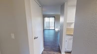 This single-story space is thoughtfully laid out, offering a cohesive blend of functional design and clean, neutral aesthetics throughout. The living area serves as the heart of the unit, featuring dark hardwood-style flooring that runs continuously through the main areas, creating a sense of visual continuity. Large vertical blinds frame a sliding glass door that floods the space with natural light and provides direct outdoor access, while an additional window further brightens the room. Crown molding adds a refined architectural detail to the living space.

A pass-through window connects the living area to the galley-style kitchen, which is efficiently organized with white cabinetry lining both sides, granite-style countertops, stainless steel appliances including a refrigerator and over-the-range microwave, and a stainless steel sink. A skylight-style ceiling fixture provides additional illumination.

The bedroom offers a comfortable, carpeted retreat with a closet and a window that brings in natural light. The bathroom is well-appointed with a full tub-shower combination, granite-topped vanity, and brushed nickel fixtures. A hallway with a closet connects the rooms, completing this efficiently designed single-floor layout.