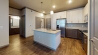 This well-appointed single-floor residence showcases a thoughtfully designed open-concept layout that seamlessly connects the kitchen and living areas. The kitchen serves as the centerpiece of the home, featuring a large central island with a granite countertop and undermount sink, pendant lighting overhead, and a two-tone cabinet scheme pairing crisp white upper cabinets with rich dark wood lower cabinets. A full suite of stainless steel appliances — including a French door refrigerator with ice dispenser, electric range, and built-in microwave — adds a polished, contemporary feel. Subway tile backsplash and wood-look flooring complete the kitchen's modern aesthetic. The bedrooms offer plush carpeting, ceiling fans, and large windows fitted with horizontal blinds that allow generous natural light while maintaining privacy. Crown molding details add a refined architectural touch throughout. The bathrooms are finished to a high standard, featuring granite-topped dark wood vanities, framed mirrors, and tiled shower-tub combinations with brushed nickel fixtures. The overall design palette of neutral tones, warm wood accents, and modern finishes creates a cohesive and inviting living environment that balances style with everyday functionality.