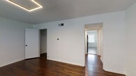 Located at 1019 W 41st Pl in Kansas City, Missouri, this single-floor unit offers a clean, well-maintained layout with a cohesive design throughout. Rich, dark hardwood flooring runs through the main living areas and bedrooms, lending warmth and character to the space. Each room is illuminated by modern geometric LED pendant fixtures that add a contemporary touch to the otherwise neutral, white-walled interiors.

The living area is open and inviting, with a front-facing window dressed in white blinds that allows natural light to fill the room. A front entry door with a window further brightens the space. The bedrooms continue the hardwood flooring aesthetic, with one room featuring a closet with built-in shelving for practical storage.

The kitchen is well-appointed with rich wood cabinetry, white quartz-style countertops, and a classic white subway tile backsplash. Black appliances, including a gas range and dishwasher, provide functional contrast, while a window above the sink brings in natural light. Light-toned tile flooring completes the kitchen's clean and practical design.

The bathroom features white tile surrounding a tub-shower combo, a wood-toned vanity with a single-basin sink, dark hardware accents, and mosaic tile flooring, creating a simple and tidy finish. Overall, the space presents a functional, updated interior with consistent finishes throughout.