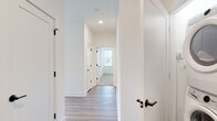 Located at 580 Columbia Tpke in East Greenbush, NY, this single-floor unit showcases a clean, modern design with high-quality finishes throughout. The open-concept kitchen and living area serves as the heart of the space, highlighted by warm wood-toned lower cabinetry paired with crisp white upper cabinets and a classic subway tile backsplash. A large central island with a quartz countertop and matte black pendant lighting anchors the kitchen, which is equipped with stainless steel appliances. The adjoining living area is bathed in natural light, courtesy of expansive windows and sliding glass doors that open to a private balcony with views of surrounding greenery. Light-toned luxury vinyl plank flooring flows seamlessly throughout the main living areas, lending warmth and continuity. A well-designed hallway connects the private quarters, featuring white panel doors accented with matte black hardware. The bathroom is outfitted with a dual-sink vanity in a natural wood finish, paired with white quartz countertops, dual framed mirrors, and modern lighting. A spacious walk-in closet with wire shelving and carpeted flooring provides generous storage. The overall ambiance is bright, airy, and contemporary, reflecting thoughtful design and attention to detail.