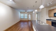 This single-story unit in Waller, Texas, offers a thoughtfully designed layout across a comfortable footprint. The open-concept living and kitchen area serves as the heart of the home, featuring warm wood-look flooring, a ceiling fan, and track lighting overhead. A built-in desk with cabinetry along one wall provides a functional workspace, while crown molding details add a refined touch to the living space.

The kitchen is well-equipped with light wood cabinetry, dark countertops, and black appliances including an electric range, microwave, and refrigerator. A central island with a built-in sink and pendant lighting above offers additional prep space and casual dining potential.

The bedroom features plush carpeting, a ceiling fan, and a window with blinds that allows natural light to filter in. It connects to a dedicated walk-in closet outfitted with dual hanging rods and a built-in shelving unit, offering ample storage.

The bathroom includes a warm wood vanity with dark countertop and single sink, tile flooring, and a generously sized soaking tub with tile surround. A hallway connects the main living areas, completing the efficient and functional floor plan.