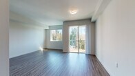 This well-appointed single-floor unit offers a clean, contemporary design with consistent hardwood-style flooring running throughout every room, creating a cohesive and polished look. The open living area is generously sized, bathed in natural light from large windows and a sliding glass door that opens onto a private balcony. From the balcony, residents enjoy peaceful views of surrounding trees, providing a refreshing natural backdrop.

The kitchen is thoughtfully equipped with white shaker-style cabinetry, stainless steel appliances including a refrigerator, electric range, and over-the-range microwave, all set against light-toned flooring that continues the unit's unified aesthetic.

The bedroom is a comfortable, well-lit space that also benefits from a sliding glass door leading to the balcony, along with an additional window that frames the wooded scenery. A hallway connects the primary living spaces to a full bathroom, which features a soaking tub and shower combination with clean white finishes. Adjacent to the bathroom is a spacious walk-in closet with built-in shelving, offering ample storage.

Throughout the unit, neutral gray and white walls provide a versatile canvas, while recessed and flush-mount lighting ensures each area is well-illuminated. The overall ambiance is modern, airy, and move-in ready.
