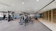 Located at 5711 John F Kennedy Blvd in North Bergen, NJ, this contemporary fitness center is designed to accommodate a wide range of workout needs within a thoughtfully organized, single-floor layout. The space is divided into distinct functional zones, each finished with purpose-appropriate flooring — durable rubberized material in the strength and cardio areas, and smooth hardwood in the open studio zone.

The main strength training area is generously sized and outfitted with a comprehensive selection of Hoist selectorized machines, free weights, benches, and cable systems. Recessed lighting throughout provides bright, even illumination across the equipment floor. A dedicated hydration station and restroom access are conveniently located within the facility.

The studio area features floor-to-ceiling mirrors, resistance bands, stability balls, and open mat space, making it ideal for stretching, functional training, or group exercise. Large windows along one wall allow natural light to fill the room and offer views of the surrounding exterior. A private cedar sauna room is accessible directly from the studio, adding a wellness-focused amenity to the space.

Glass partition walls provide visual openness between sections while maintaining defined areas. The overall aesthetic is clean and modern, with teal accent walls and a neutral palette that creates a focused, professional atmosphere throughout.