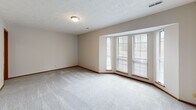 This single-floor residence offers a functional and well-organized layout with a neutral color palette and consistent finishes throughout. The expansive living room serves as the central gathering space, featuring plush carpeting, a textured ceiling, a tiled fireplace with a glass-front surround, and sliding glass doors fitted with vertical blinds that open to a private balcony, allowing natural light to filter in.

The galley-style kitchen is efficiently designed with warm oak cabinetry lining both walls, white countertops, a stainless steel sink, and black appliances including an electric range and dishwasher. Light wood-look flooring runs underfoot, and an open passageway connects the kitchen directly to the living area.

The bedrooms are carpeted and bright, with one featuring a wide bank of windows that draws in ample natural light and another offering a sliding wood-panel closet. A generously sized walk-in closet with built-in shelving and hanging rods provides substantial storage.

Two bathrooms serve the unit. The full bathroom includes wood-look flooring, a single-sink vanity with light cabinetry, and a full tub-shower combination. A secondary half-bath features a matching vanity, large mirror, and wood-look flooring, maintaining the cohesive design found throughout the space.
