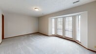 This single-floor residence offers a functional and well-organized layout with a neutral color palette and consistent finishes throughout. The expansive living room serves as the central gathering space, featuring plush carpeting, a textured ceiling, a tiled fireplace with a glass-front surround, and sliding glass doors fitted with vertical blinds that open to a private balcony, allowing natural light to filter in.

The galley-style kitchen is efficiently designed with warm oak cabinetry lining both walls, white countertops, a stainless steel sink, and black appliances including an electric range and dishwasher. Light wood-look flooring runs underfoot, and an open passageway connects the kitchen directly to the living area.

The bedrooms are carpeted and bright, with one featuring a wide bank of windows that draws in ample natural light and another offering a sliding wood-panel closet. A generously sized walk-in closet with built-in shelving and hanging rods provides substantial storage.

Two bathrooms serve the unit. The full bathroom includes wood-look flooring, a single-sink vanity with light cabinetry, and a full tub-shower combination. A secondary half-bath features a matching vanity, large mirror, and wood-look flooring, maintaining the cohesive design found throughout the space.