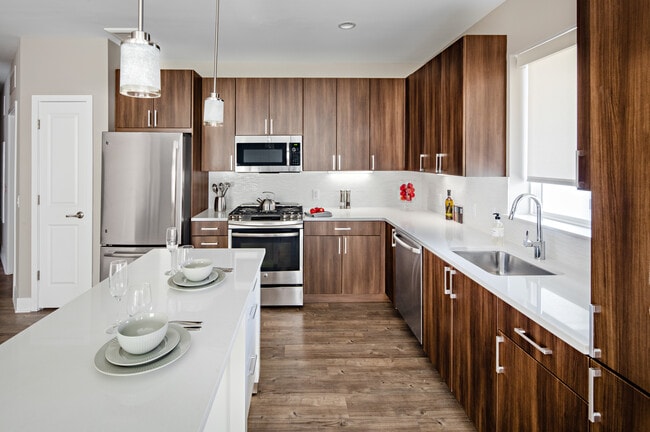 Signature Collection Kitchen with oak cabinetry, light grey quartz countertops, white tile backsplash, upgraded stainless steel appliances, and hard surface plank flooring - Avalon Princeton