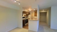 This single-floor residence at Spring House On The Park offers a thoughtfully designed open-concept layout that connects the kitchen and living areas. The kitchen is well-appointed with rich dark wood cabinetry providing ample storage, a white electric range, and a full-size refrigerator. A peninsula with a built-in sink and generous counter space serves as a natural divider between the kitchen and the adjacent living area, making it an ideal spot for casual dining or meal preparation. Track lighting throughout the space provides adjustable, focused illumination, complementing the recessed ceiling lights that brighten the hallway and entry areas. The living area features neutral-toned carpet, contributing to a warm and comfortable atmosphere, while the kitchen transitions to hardwood-style flooring for easy maintenance. The entryway, visible from the main living space, features a standard door with a straightforward, functional design. The light, neutral wall tones throughout the unit create a clean, versatile backdrop. Overall, the space offers a practical and cohesive environment well-suited for everyday living.