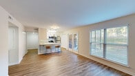 Located at 1200 Trillium Cir in Raleigh, NC, this 2-bedroom, 2-bathroom single-floor home offers a well-organized layout designed for comfortable everyday living. The open-concept living and dining area is anchored by warm wood-look flooring that flows throughout the home, while large windows and a glass patio door invite abundant natural light and provide views of the surrounding greenery. The kitchen is a standout feature, outfitted with white shaker cabinetry, granite-style countertops, a full suite of stainless steel appliances including a refrigerator, range, microwave, and dishwasher, and a breakfast bar with pendant lighting — ideal for both cooking and casual dining. A hallway connects the main living areas to the private quarters. The generously sized primary bedroom includes multiple closets with bifold doors, offering ample storage. The second bedroom is bright and airy, featuring a window with outdoor views. Both bathrooms are well-appointed, with one featuring a tiled tub-shower combination and granite countertops. Additional conveniences include a dedicated laundry area, utility room, and multiple closets throughout. The home presents a clean, neutral palette throughout, creating a bright and move-in-ready atmosphere.