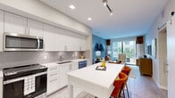 This single-story residence at Mayla in Pompano Beach, Florida, offers a thoughtfully designed one-bedroom, one-bathroom layout with modern finishes throughout. The open-concept kitchen is a standout feature, showcasing floor-to-ceiling white shaker cabinetry, a grey subway tile backsplash, quartz countertops, and a full suite of stainless steel appliances including a gas range, microwave, and dishwasher. A generous kitchen island with bar seating serves as a natural focal point and seamlessly connects to the living area.

The living room is bright and welcoming, with large sliding glass doors that open to a private balcony, allowing natural light to fill the space and providing views of the surrounding outdoor setting. Light wood-style flooring runs throughout, lending warmth and continuity to the open layout.

The bedroom is a calm retreat, featuring a walk-in closet with built-in shelving and direct access to the bathroom. The bathroom is finished with floor-to-ceiling neutral tile surrounding a full soaking tub and shower combination. Recessed lighting, track lighting accents, and neutral tones throughout contribute to the residence's clean, contemporary ambiance.