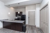 This single-floor residence at 10063 S Creek Run Way in Sandy, Utah, offers a well-organized layout designed for comfortable everyday living. The open-concept kitchen and living area serves as the heart of the unit, where wood-look plank flooring extends throughout, creating a cohesive and clean aesthetic. The kitchen is equipped with dark cabinetry, granite-style countertops, a built-in sink, pendant lighting, and black appliances including a refrigerator, range, and over-the-range microwave. Track lighting overhead provides practical illumination, while a sliding window brings in natural light from an adjacent patio or balcony area.

The living space flows seamlessly from the kitchen, with neutral walls and elevated ceilings contributing to an open, airy feel. Bedrooms are carpeted for warmth and comfort, each featuring windows with blinds that admit natural light, and ceiling fans for climate control. Closet space is generous, with at least one walk-in closet featuring built-in rod and shelf storage.

The bathrooms are finished with wood-look flooring, granite-topped vanities with dark cabinetry, and include both a shower/tub combination and a separate walk-in shower, offering practical flexibility. The overall palette of neutral tones throughout gives the space a clean, move-in-ready appearance.