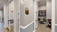 Located at 3055 Riverbirch Dr in Aurora, Illinois, this single-floor professional office suite offers a polished and functional environment designed for productivity and collaboration. The space is characterized by consistent architectural detailing throughout, including crown molding, white chair-rail wainscoting with a two-tone gray and taupe color palette, and wood-look tile flooring in the corridors that transitions to neutral carpeting in the offices.

The centerpiece of the suite is a formal conference room featuring a large, high-gloss cherry wood conference table surrounded by executive leather chairs. Tall, multi-pane windows flood the room with natural light and frame views of lush greenery outside, while framed artwork adorns the walls, lending a refined, professional atmosphere. Crown molding and elevated ceilings further enhance the room's sense of scale.

A dedicated business center provides built-in cherry wood desks, ergonomic task chairs, and wall-mounted glass-door cabinetry, offering functional workstations for focused tasks. The well-lit corridors connect multiple areas seamlessly, with glass-panel doors, recessed lighting, and glimpses of a fitness area, adding versatility to the overall space. Decorative brass signage accents the hallways, contributing to the suite's classic, upscale character throughout.