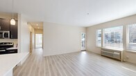 This single-floor, 2-bedroom, 2-bathroom residence is thoughtfully designed to maximize functionality and comfort. The open living area serves as the heart of the unit, finished with light-toned hardwood-style flooring that runs throughout the main spaces. Large windows and a glass exterior door bathe the room in natural light while providing access to an outdoor balcony area, creating a bright and airy ambiance. A wall-unit HVAC system ensures year-round climate control.

The kitchen is a standout feature, showcasing dark espresso cabinetry that extends to the ceiling for ample storage, contrasted by crisp white quartz countertops. A central island with a built-in sink adds both prep space and a casual dining option, while stainless steel appliances—including a refrigerator, electric range, and built-in microwave—complete the modern aesthetic.

Both bedrooms are carpeted for warmth and comfort. The primary bedroom includes a spacious walk-in closet fitted with wire shelving and hanging rods. The second bedroom features a sliding-door closet with dedicated hanging storage. A hallway bathroom and a second bathroom near the laundry area—which houses a full-size washer and dryer—provide added convenience. Neutral tones and clean finishes throughout lend the space a cohesive, contemporary character.