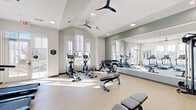 Located at 7800 Creekridge Rd in Charlotte, NC, this fitness center offers a bright and well-appointed space designed to support a comprehensive workout routine. The room features vaulted ceilings with dual ceiling fans and recessed lighting, creating an airy, open atmosphere throughout. Large windows line multiple walls, flooding the space with abundant natural light and providing views of the surrounding outdoor scenery, while roller shades allow for adjustable privacy.

The cardio zone is well-stocked with multiple treadmills, elliptical trainers, and a stationary bike, all positioned to take advantage of the natural light from the expansive windows. A strength training area includes adjustable weight benches, a multi-function cable machine, dumbbells, medicine balls, and resistance accessories neatly organized on dedicated racks.

A large floor-to-ceiling mirror spans one wall, visually expanding the space and aiding in form correction during workouts. An accent wall featuring a bold botanical wallpaper adds a distinctive design element, complemented by framed artwork placed throughout the room. The durable speckled flooring is well-suited for high-traffic fitness use. A glass door provides direct access to an outdoor area, further enhancing the sense of openness and connectivity to the exterior environment.