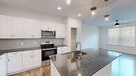 This well-appointed one-bedroom, one-bathroom residence in South Fulton, Georgia, offers a thoughtfully designed single-floor layout that maximizes functionality and modern style. The kitchen serves as a centerpiece, showcasing dark granite countertops atop crisp white shaker cabinetry, a subway tile backsplash, and a full suite of stainless steel appliances including a French door refrigerator, electric range, and over-the-range microwave. A kitchen island with an undermount sink provides additional prep space and is accented by pendant lighting overhead. Wood-look plank flooring runs through the main living areas, lending warmth to the bright, open layout that connects the kitchen to the dining and living areas. The bedroom is a comfortable, well-proportioned retreat featuring plush carpet, a ceiling fan, and a window with outdoor views of surrounding greenery. Direct access leads to a spacious walk-in closet equipped with wire shelving and hanging racks for ample storage. The bathroom features tile flooring, a granite-topped vanity with white cabinetry, and a glass-enclosed shower, maintaining the same refined aesthetic found throughout the home.