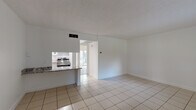 Located at 7655 NW 42nd Pl in Sunrise, Florida, this single-story unit presents a clean, functional layout with a bright, neutral palette throughout. The main living area is generously proportioned, featuring light-toned ceramic tile flooring and a textured ceiling that adds subtle visual interest. White walls and natural light filtering in from a window and nearby balcony access contribute to an open, airy atmosphere. A secondary living or flex space near the entry shares the same tile flooring and benefits from a window overlooking the outdoors.

The kitchen is efficiently designed and opens toward the living area via a peninsula counter finished in granite, providing a practical workspace and casual dining option. White cabinetry with glass-front uppers offers ample storage, while a stainless steel range with overhead ventilation hood anchors the cooking space. Tile flooring continues seamlessly through the kitchen.

The bedroom features light wood-tone laminate flooring and a sliding glass door that leads to a private balcony, allowing for natural light and outdoor access. The bathroom is finished with wood-tone laminate flooring, white shaker-style cabinetry, and a light stone-finish countertop, maintaining the cohesive, clean aesthetic found throughout the space.