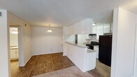 This single-floor residence offers a well-organized, functional layout designed for comfortable everyday living. The entryway, finished with warm wood-look flooring, welcomes you into the home and provides access to a closet, setting a clean and practical tone throughout.

The open-concept kitchen and living area serves as the heart of the home. The kitchen features white cabinetry, granite-style countertops, a tiled backsplash, and black appliances including a range and refrigerator. A peninsula with a breakfast bar visually connects the kitchen to the dining and living spaces, where a pendant light and built-in shelving add character and utility. The transition between wood-look flooring and plush carpet marks the shift into the living area.

The living room is generously proportioned, with a striking stone fireplace as its focal point. Large windows and a set of French doors flood the room with natural light and provide direct access to an outdoor patio area. A ceiling fan with a light kit completes the space.

The bedroom is carpeted and features a walk-in closet with built-in shelving, offering ample storage. The bathroom is well-appointed with a granite-style vanity countertop, white cabinetry, a full tub-shower combination, and a large mirror with overhead lighting — delivering a clean, bright finish throughout.