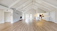 Located at 1080 Cimarron Cir in Aurora, CO, this single-floor space makes a striking architectural impression through its dramatic vaulted ceiling adorned with white-painted exposed wooden beams and shiplap, creating an airy, expansive atmosphere that feels far larger than its footprint suggests. Ceiling fans are thoughtfully positioned throughout to complement the soaring roofline.

The open-concept layout seamlessly unites the living area and kitchen into one cohesive space. The living room is anchored by a full-height whitewashed brick fireplace wall featuring an arched firebox and a floating hearth shelf, serving as the room's defining focal point. Light hardwood flooring runs throughout, lending warmth and continuity across the entire floor plan. Multiple windows and glass-paneled doors flood the interior with abundant natural light while offering views of the surrounding outdoors.

The kitchen is well-appointed with crisp white shaker cabinetry, clean quartz countertops, and a full suite of stainless steel appliances including a gas range, over-the-range microwave, and refrigerator. A generous peninsula provides additional prep space and creates a natural transition between the kitchen and living areas. Recessed lighting above the kitchen ensures a bright, functional workspace that complements the overall light-filled ambiance of this thoughtfully designed space.