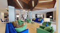 This single-floor amenity space makes a strong first impression with a welcoming entrance lobby featuring large-format hexagonal tile flooring, a statement lounge chair, lush tropical plants, and glass entry doors that invite abundant natural light. The interiors are defined by a bold, contemporary design palette — rich cobalt blue sofas, vibrant emerald green armchairs, and striking leopard-print accent pillows and ottomans create an energetic, resort-inspired atmosphere throughout.

The main lounge area is a standout, anchored by a distinctive slatted wood ceiling installation with integrated linear lighting that adds warmth and architectural depth. A gold geometric coffee table serves as a focal point, surrounded by plush seating arrangements ideal for casual gatherings. Mirrored wall panels and open sightlines enhance the sense of spaciousness throughout this area.

A second lounge zone features a dramatic dark brick fireplace wall with a mounted television, complemented by leopard-print accent chairs, a sculptural coffee table, and curated artwork — offering a more intimate setting for relaxation.

The kitchenette and bar area is thoughtfully designed with a curved gray quartz island, white and green Greek key barstools, soft blue patterned tile backsplash, gray cabinetry, a beverage refrigerator, and geometric pendant lighting. An adjacent flat-screen television and open views toward a fitness area make this a functional and social hub for residents and guests.