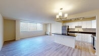 Located at 4400 E West Hwy in the heart of Bethesda, MD, this well-appointed single-floor residence offers a thoughtfully designed open-concept layout that seamlessly connects the living, dining, and kitchen areas. Light wood-style flooring runs throughout the space, lending a clean, contemporary feel to every room.

The expansive living area is bathed in natural light through a large picture window with views of the surrounding urban streetscape, and features a textured ceiling and a wall-mounted HVAC unit. An elegant chandelier anchors the dining zone, which flows effortlessly into the kitchen.

The kitchen is a standout feature, outfitted with crisp white shaker cabinetry, rich dark granite countertops, a peninsula with seating potential, and a full suite of stainless steel appliances including a gas range, built-in microwave, refrigerator, and dishwasher. Track lighting overhead ensures the workspace is well-illuminated.

The bedroom offers generous storage with two side-by-side reach-in closets, providing ample organization space. The bathroom is finished with large-format neutral tile surrounding a full soaking tub and shower combination, complemented by brushed nickel fixtures for a polished look throughout.