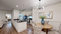 This single-story residence features two bedrooms, two bathrooms, and a thoughtfully designed open layout that connects the kitchen, dining, and living areas seamlessly. The kitchen is equipped with stainless steel appliances, dark granite countertops, a subway tile backsplash, and grey shaker-style cabinetry. A peninsula with an undermount sink and matte black faucet extends into the dining area, creating a practical workspace and casual gathering point. The dining area features crown molding, wood-look flooring, and a modern sputnik chandelier overhead.

The living room connects to a built-in media niche with cabinetry and open shelving, maintaining a clean and organized aesthetic. Wood-look flooring runs throughout the main living areas, while plush carpet is found in both bedrooms. The primary bedroom includes a ceiling fan, access to natural light through large windows, and a generously sized closet. The secondary bedroom offers a comfortable, well-lit retreat. Both bathrooms feature dark granite vanity tops, light wood cabinetry, and matte black hardware. A dedicated in-unit laundry area with washer and dryer hookups and overhead shelving adds everyday convenience.