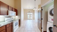 Located at 5 E Columbia Ave in Champaign, Illinois, this single-floor residence offers a thoughtfully designed layout with a bright, open feel throughout. The combined kitchen and dining area is a standout feature, boasting impressively high ceilings, light-toned tile flooring, and dual chandelier lighting that adds an elegant touch. The kitchen is equipped with wood-toned cabinetry, a white electric range, and a built-in microwave, while the adjacent dining space opens to the exterior through a set of glass French doors, filling the area with natural light. The bedrooms are finished with plush carpeting and elevated ceilings, each offering generous walk-in closet space with built-in wire shelving systems accessed through paneled wood doors. Natural light filters in through window blinds, enhancing the warm, neutral color palette of the walls. The bathroom is well-appointed with classic hexagonal mosaic tile flooring in white, soft sage-green walls, a pedestal sink, a wood vanity with countertop storage, an oil-rubbed bronze light fixture and mirror, and a framed walk-in shower. Overall, the space presents a clean, functional, and comfortable living environment with consistent warm-toned finishes throughout.