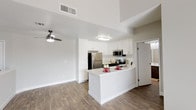 Located at 22900 Oak Ridge Dr in Santa Clarita, California, this single-story residence offers a clean, modern aesthetic throughout its well-designed floor plan. The open-concept living area is immediately striking, featuring soaring vaulted ceilings and rich, dark hardwood-style flooring that flows seamlessly through the main living spaces. A large sliding glass door floods the living room with natural light while providing access to an outdoor balcony area and views of the surrounding greenery.

The kitchen is thoughtfully designed with white shaker-style cabinetry, light quartz countertops, and a peninsula that doubles as a breakfast bar. Stainless steel appliances — including a refrigerator, gas range, and built-in microwave — complement the two-toned cabinetry, with darker lower cabinets providing a modern contrast. A ceiling fan in the adjacent living area enhances comfort and airflow.

The bedrooms feature plush wall-to-wall carpeting and tall ceilings that lend a spacious feel. Natural light enters through slatted blinds, and at least one bedroom includes mirrored sliding closet doors. The bathroom is clean and functional, outfitted with a full tub-and-shower combination featuring chrome fixtures and a curved shower rod. The overall palette of soft neutrals and white trim creates a bright, welcoming atmosphere throughout.