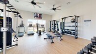 The Yardly Beltmill Fitness Center, located in Saginaw, TX, is a thoughtfully designed exercise facility that delivers a comprehensive workout experience within a bright, welcoming space. The single-room layout features light wood-style flooring, neutral walls, and vaulted ceilings with dual ceiling fans that promote airflow and comfort throughout workouts.

Natural light floods the room through large sliding glass windows and doors, offering views of the surrounding neighborhood and creating an open, energizing atmosphere. Wall-mounted flat-screen televisions are positioned at multiple angles, ensuring entertainment or instructional content is easily visible from anywhere in the room.

The fitness center is equipped with an impressive selection of commercial-grade equipment. Cardio offerings include a treadmill, elliptical trainer, and stationary cycle, all positioned to take advantage of the natural light. For strength training, the space features a cable machine system, a power rack loaded with weight plates and a barbell, adjustable benches, and a full dumbbell rack. A dedicated functional training station includes TRX suspension trainers, resistance bands, medicine balls, stability balls, foam rollers, and a wall-mounted storage rack to keep accessories organized.

Wall mirrors amplify the sense of space and allow for form checks during exercise. The prominently displayed "Yardly Beltmill" branding adds a polished, community-focused identity to this well-appointed fitness amenity.