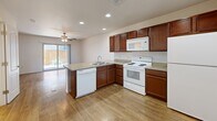 Located in El Paso, TX, this two-story, two-bedroom, three-bathroom home offers a practical and well-appointed layout spread across two floors. The ground floor hosts the main living and kitchen area, where rich dark-wood cabinetry pairs with granite-style countertops and a peninsula island that provides additional prep and seating space. White appliances, including a range, microwave, dishwasher, and refrigerator, complete the kitchen. Recessed lighting and wood-look plank flooring add warmth and brightness throughout the main level. A sliding glass door in the kitchen area opens to an outdoor view, allowing natural light to flow in. A staircase connects the two floors, leading to the upper level where both bedrooms are situated. Each bedroom features plush carpeting, ceiling fans with light fixtures, and windows that invite natural light. The primary bedroom includes a dedicated closet, while the second bedroom offers ample built-in closet storage. Three bathrooms serve the home, each featuring wood-look flooring, a tub-shower combination with built-in shelving, and rich wood-toned vanities with stone-style countertops. The overall aesthetic is clean, neutral, and functional throughout.