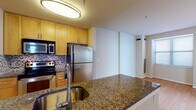 This single-floor residence offers a cohesive and functional layout with consistent finishes throughout. The kitchen serves as a central highlight, featuring a peninsula with dark granite countertops, an undermount sink, and light maple cabinetry extending to the ceiling for ample storage. Stainless steel appliances, including a refrigerator, range, and built-in microwave, are complemented by a herringbone-patterned tile backsplash. A circular flush-mount light fixture illuminates the space.

Light hardwood-style flooring flows throughout the main living areas and into the bedrooms, creating visual continuity. One bedroom features a window with horizontal blinds allowing natural light, while another room benefits from a skylight panel overhead. A dedicated closet area with built-in shelving provides organized storage.

The hallway connects rooms with a clean, neutral palette of warm beige tones and white trim. The full bathroom features dark tile flooring, a tub-shower combination with tiled surround, a maple vanity with granite countertop, an undermount sink, and a large mirror with a multi-bulb light fixture above. The overall design is practical and uniform, with a calm, neutral aesthetic throughout.