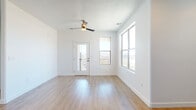 This single-floor unit offers a clean, contemporary design highlighted by light hardwood-style flooring that runs consistently throughout every room. The open living area is bright and airy, benefiting from large windows that frame outdoor views of the surrounding cityscape and distant mountains. A ceiling fan with a modern finish provides both function and style overhead, while a textured ceiling adds subtle visual interest. A glass-paneled exterior door leads to a private balcony, further enhancing the connection to the outdoors and allowing natural light to flood the space.

The kitchen is well-appointed with dark wood-grain cabinetry, light speckled stone countertops, and a full suite of black appliances, including a refrigerator, electric range, built-in microwave, and dishwasher. Recessed lighting illuminates the workspace effectively, and a window above the sink brings in additional natural light. The layout flows openly toward the living area, making the space feel connected and functional.

The bedroom features multiple closet doors, offering generous storage, while the bathroom includes a wood-grain vanity, speckled stone countertop, a large mirror, and matching fixtures consistent with the unit's modern aesthetic. The overall ambiance is clean, minimal, and move-in ready.