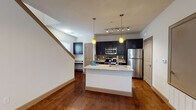 This two-story residence is designed with a cohesive blend of modern finishes and functional layouts. The main level centers around an open-concept kitchen and living area, where rich hardwood flooring flows throughout. The kitchen is well-appointed with dark cabinetry, a mosaic tile backsplash, stainless steel appliances including a refrigerator, range, and microwave, and a central island featuring granite countertops with an undermount sink. Pendant lighting with warm yellow glass shades and a track lighting system illuminate the space effectively. A dedicated entry area with a front door and adjacent windows provides natural light to the lower level.

The upper floor hosts multiple bedrooms, each finished with plush neutral carpeting, ceiling fans, and windows fitted with horizontal blinds that allow natural light while maintaining privacy. The bedrooms are generously proportioned with clean, neutral walls. Two bathrooms serve the residence: one full bath featuring a double-sink granite vanity, dark cabinetry, a shower, and a tub with natural light from windows, and a second bath with a single granite vanity, dark-framed mirror, and wood-look flooring. Throughout, the consistent use of granite surfaces, dark cabinetry, and quality finishes creates a unified, contemporary aesthetic.