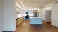 Located at 9800 Mira Lee Way in San Diego's Mira Mesa neighborhood, this single-floor residence showcases a clean, contemporary design throughout. The open-concept kitchen is a standout feature, outfitted with warm wood-tone lower cabinetry, sleek gray upper cabinets, white quartz countertops, and a large central island. Stainless steel appliances — including a refrigerator, range, microwave, and dishwasher — complement the modern aesthetic, while pendant lighting and recessed fixtures provide a well-lit environment. Rich hardwood-style flooring extends through the kitchen and flows seamlessly into the spacious living area, which is bathed in natural light from sliding glass doors that open to a private balcony with outdoor views. The bedrooms offer plush carpeting, ceiling fans, and ample space, with generous closet access. The bathroom features light tile flooring, a wood-tone vanity with white countertop, a large mirror, and a tub-shower combination. Throughout the residence, neutral wall tones and consistent modern finishes create a cohesive, inviting atmosphere well-suited to comfortable everyday living in San Diego.
