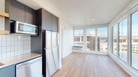 This well-appointed one-bedroom, one-bathroom unit offers a thoughtfully designed single-floor layout that maximizes both function and comfort. Warm hardwood-style flooring flows continuously throughout the entire space, creating a cohesive and inviting aesthetic.

The open-concept living area is a standout, featuring expansive floor-to-ceiling corner windows that flood the room with natural light and frame sweeping panoramic city views. The kitchen is sleek and modern, outfitted with dark gray flat-panel cabinetry, a gas range with a stainless steel hood, a built-in microwave, dishwasher, and stainless steel refrigerator, all complemented by a crisp white subway tile backsplash and light countertops.

The bedroom is a bright, private retreat with wide horizontal windows offering additional urban views and a dedicated closet for ample storage. The bathroom continues the contemporary design language, featuring gray cabinetry, a clean white countertop with an undermount sink, and a full mirror. A stacked washer and dryer unit is conveniently housed within the bathroom, adding practical in-unit laundry. Clean white walls throughout keep the space feeling open, fresh, and move-in ready.