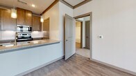 This single-floor residence presents a cohesive, contemporary design highlighted by warm wood-tone cabinetry, granite countertops, and light wood-look flooring throughout the main living areas. The kitchen is well-appointed with stainless steel appliances, including a range with overhead microwave, dishwasher, and refrigerator, complemented by a subway tile backsplash and a peninsula that provides additional counter space and casual seating. Pendant lighting adds a refined touch above the kitchen area. A dedicated laundry space with side-by-side washer and dryer connections is conveniently accessible directly from the kitchen corridor.

The bedrooms feature plush carpeting and are filled with natural light through large windows fitted with horizontal blinds. One bedroom benefits from multiple windows on two walls, while another includes a ceiling fan and neighborhood views. Walk-in closets with built-in wire shelving provide organized storage. The primary bathroom features a wide double-sink vanity with granite countertops, a large mirror, and a tub-shower combination set on wood-look flooring. A second full bathroom mirrors the same finishes with a single-sink vanity and tiled tub surround. Crown molding and neutral tones throughout create a clean, move-in-ready environment.