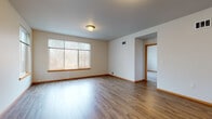 This single-floor unit offers a thoughtfully designed layout with a clean, neutral aesthetic throughout. The open living area is finished with warm hardwood-style flooring, cream-toned walls, and wood-trimmed windows that allow natural light to filter in, with views of surrounding greenery. The space flows seamlessly between the main living area and connecting rooms via open archways and wood-trimmed doorways.

The kitchen features medium-toned wood cabinetry with sleek bar-pull hardware, stone-look countertops, and black appliances including a range and microwave, complemented by hardwood-style flooring and a window that brings in additional natural light.

Bedrooms are finished with plush carpeting and generous windows. One bedroom includes a walk-in closet with built-in shelving, while another features wide windows overlooking the surrounding landscape.

Two bathrooms serve the unit. The first is a full bath with a tub-shower combination, wood vanity, stone-look countertop, and hardwood-style flooring. The second is an accessibility-equipped bathroom featuring grab bars, a fold-down shower seat, and a handheld showerhead. In-unit laundry is conveniently located nearby.