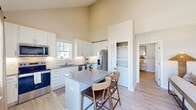 Located at 26 Mullein Dr in Hampstead, NC, this two-story, 2-bedroom, 2-bathroom home offers a clean, modern design with functional living spaces spread across two well-proportioned floors. The main level features an open-concept kitchen and living area with soaring ceilings that amplify the sense of space. The kitchen is outfitted with white shaker-style cabinetry, quartz countertops, a herringbone tile backsplash, stainless steel appliances — including a side-by-side refrigerator — and a central island with seating. Light wood-look flooring runs throughout the main level, complementing the bright, neutral palette. The living room benefits from natural light through large windows with views of the surrounding neighborhood. Upstairs, the primary bedroom is a comfortable retreat with plush carpeting, natural light, and an en-suite bathroom featuring a sleek frameless glass walk-in shower with white subway tile. A well-organized walk-in closet with built-in shelving and dual hanging rods serves the primary suite. The second bedroom is airy and bright, also with light-filled windows. A second full bathroom includes a tub-shower combination with classic white subway tile surround. The home's layout and finishes reflect a consistently modern, move-in-ready aesthetic throughout.