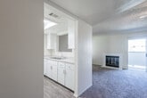 This single-floor residence offers a practical and comfortable layout designed for everyday living. The spacious living room serves as the heart of the home, featuring plush carpeting, a textured ceiling, and a ceiling fan with integrated lighting. A white-tiled fireplace adds a classic focal point to the room, while a sliding glass door with vertical blinds provides access to an outdoor area and fills the space with natural light. The open layout connects the living area to a well-appointed kitchen, which features white cabinetry, a double-basin sink, and ample counter space, all complemented by wood-look flooring for easy maintenance. A pass-through or open partition visually links the kitchen to the adjoining dining or entry area, enhancing the sense of openness throughout. The bedroom is a quiet, well-lit retreat with carpeted floors, neutral walls, and a window fitted with blinds for privacy and light control. The bathroom is clean and functional, outfitted with a full tub-and-shower combination featuring a curved curtain rod, grab bar, and wood-look flooring. Throughout the home, a neutral color palette and textured ceilings create a cohesive, understated aesthetic that is move-in ready and easy to personalize.